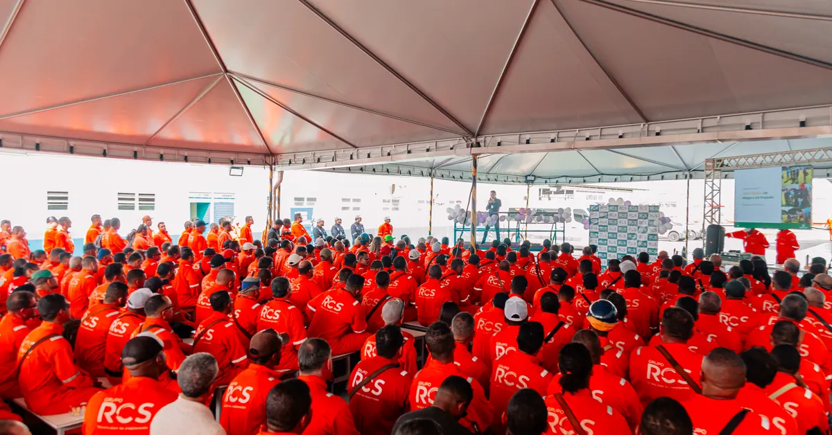 Centenas de trabalhadores de uniforme laranja reunidos sob a tenda do evento, voltados ao palco.